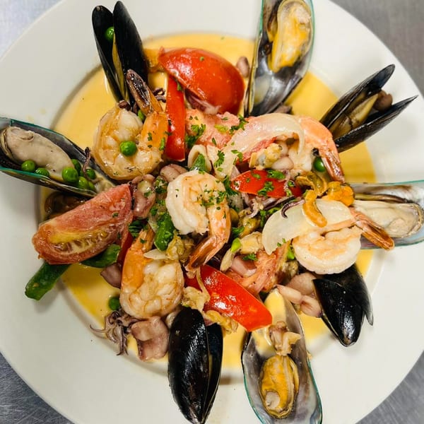 A vibrant seafood dish with mussels, shrimp, and vegetables in a creamy sauce, served on a white plate.