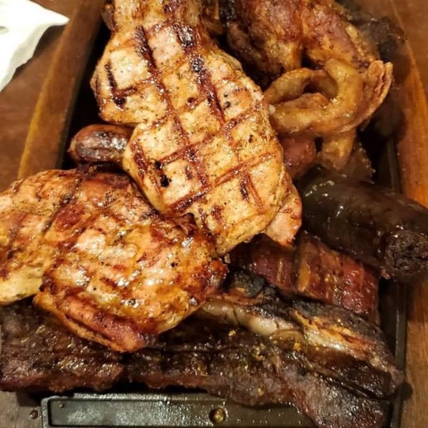 Close-up of a sizzling platter of various grilled meats, including steaks, sausages, and blood sausage.