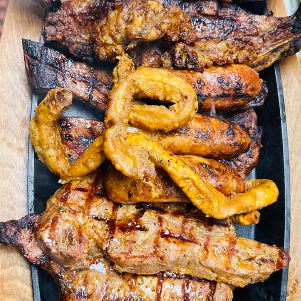 Close-up of a sizzling platter of Argentinian grilled meats, including steak, sausages, and chinchulines.